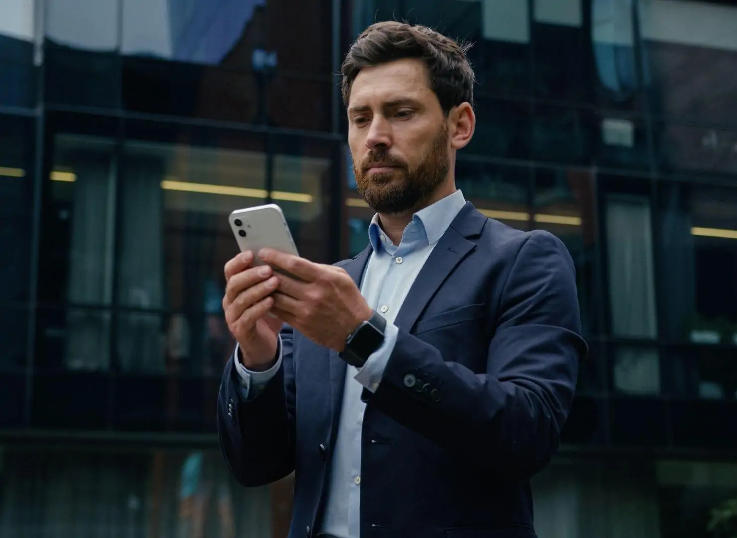 Homem de negócios focado lendo informações no celular em frente a um prédio corporativo. Representa o acesso à Carta Mensal de finanças da Value Capital.
