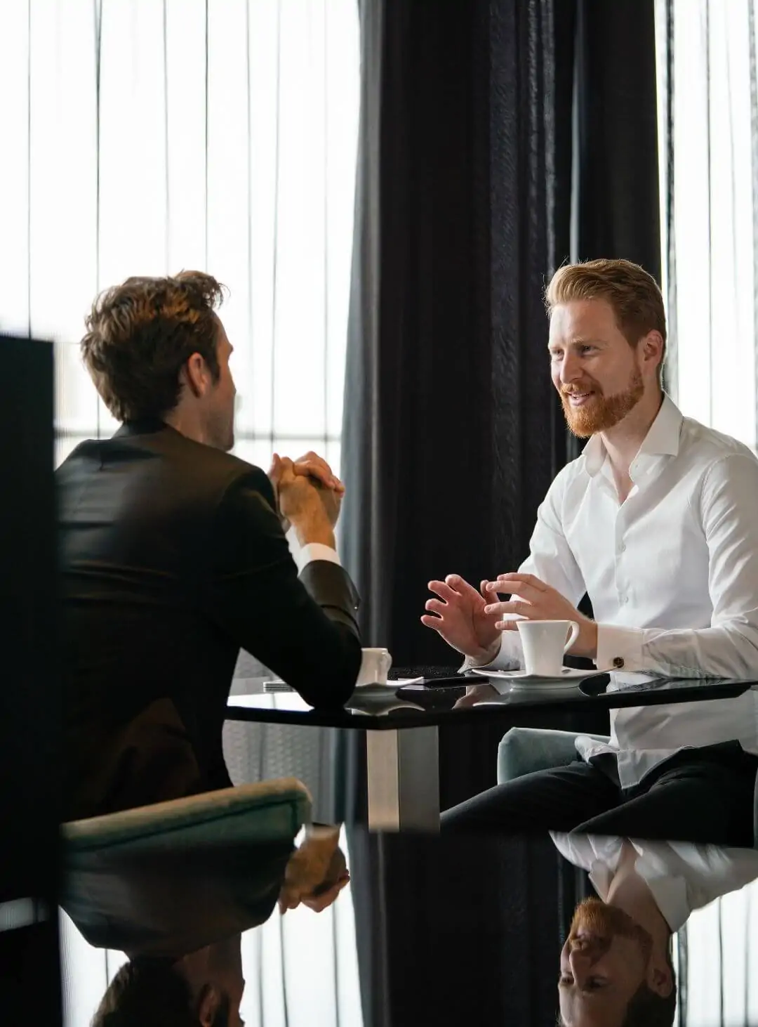 Dois executivos em uma reunião de negócios amigável tomando café. Ilustra a conexão entre empresas da economia real e investidores qualificados pela Value Securitizadora.