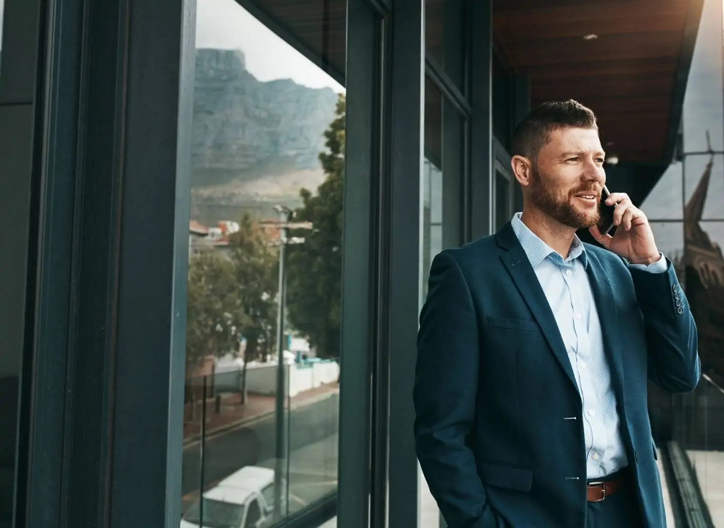 Homem de negócios com terno azul falando ao celular em frente a um prédio comercial moderno. Ilustra o card de apresentação da Value Capital como boutique de finanças.