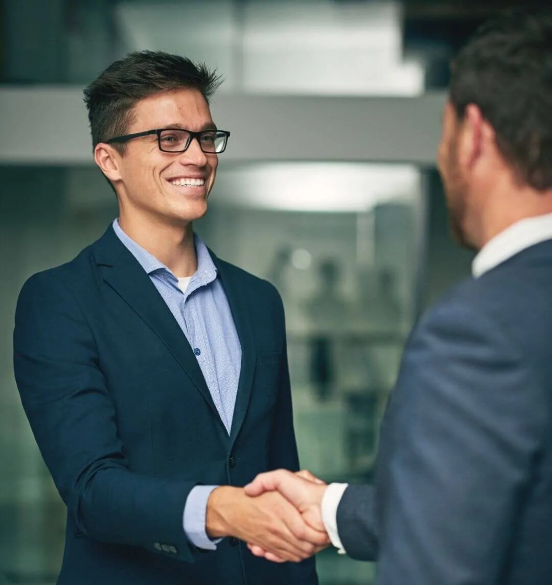 Dois executivos sorridentes se cumprimentando com um aperto de mãos em um escritório corporativo iluminado. Representa a visão integrada de confiança entre a gestão da empresa e os sócios.